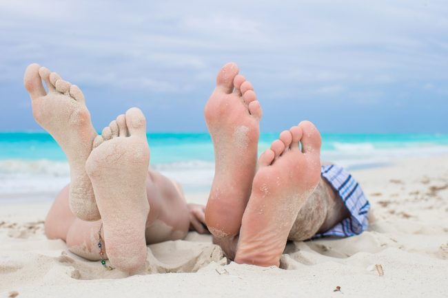 Close up male and female feet on white sand beach