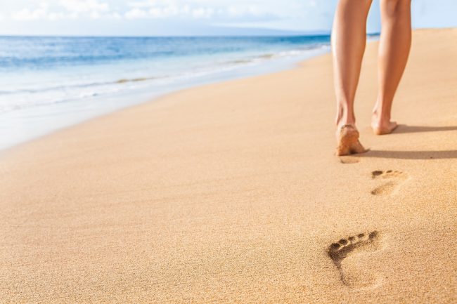 Beach travel - woman relaxing walking on sand beach leaving foot