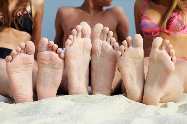 Soles of teenagers sunbathing on sandy beach